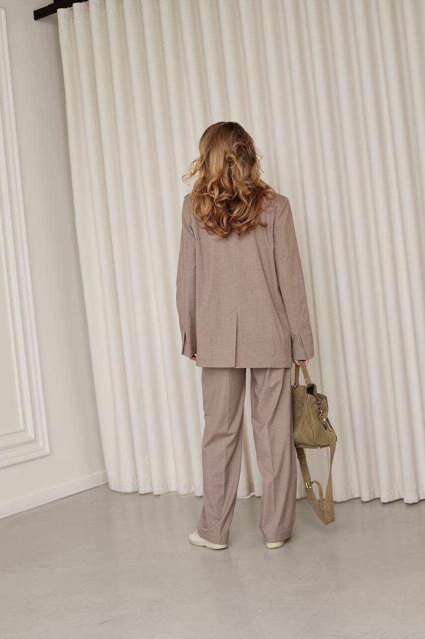 Woman in a pink suit standing in front of white curtains