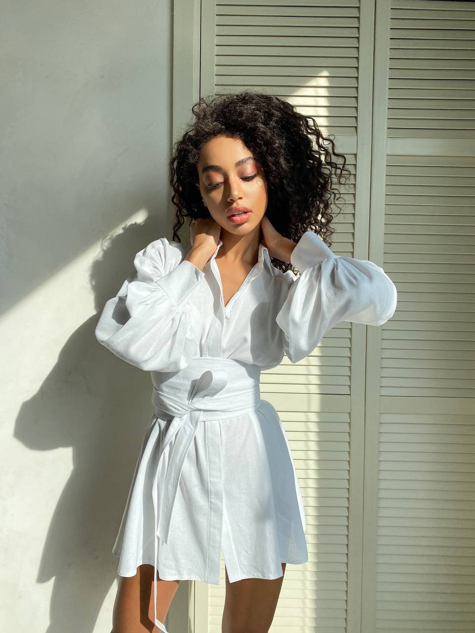 Woman wearing a white outfit standing against a light-colored wall.