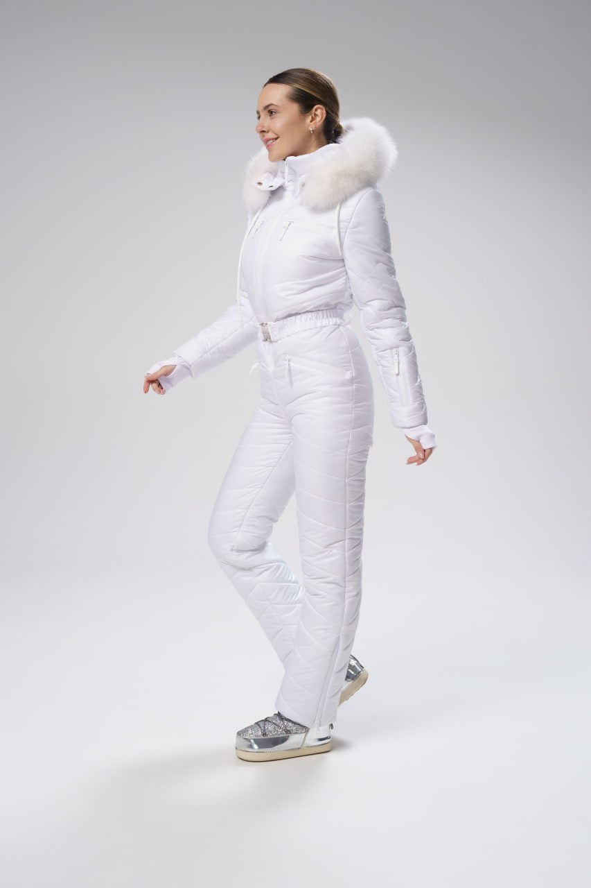 Woman wearing a white snowsuit with fur hood on a gray background