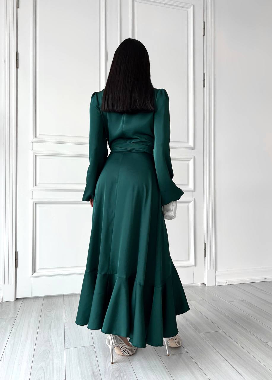 Woman wearing a long green dress standing in a room with white walls and wooden floor.