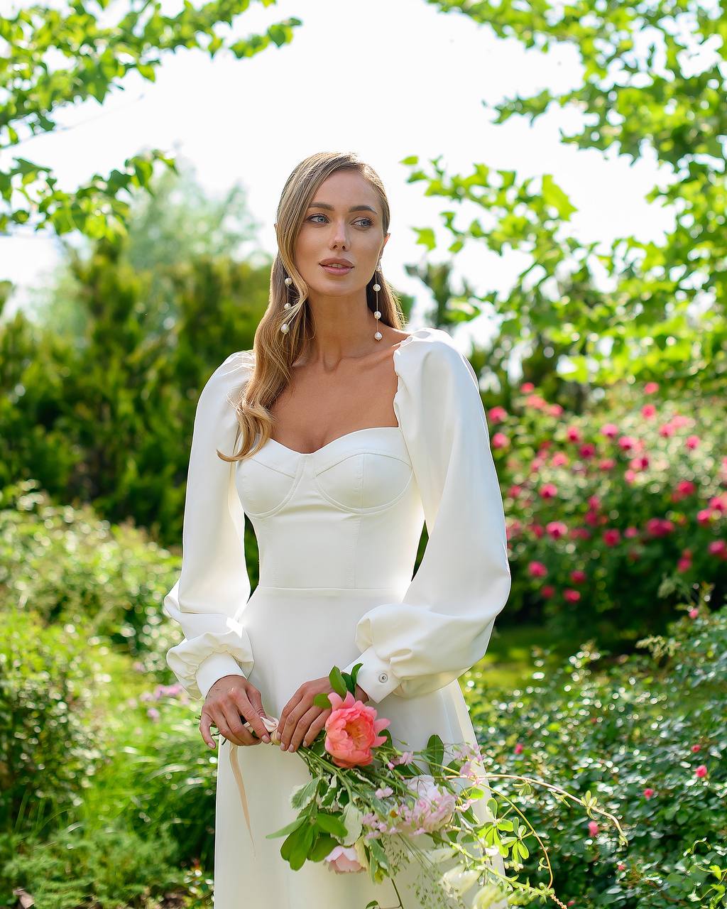 Woman in a white wedding dress holding flowers in a garden setting