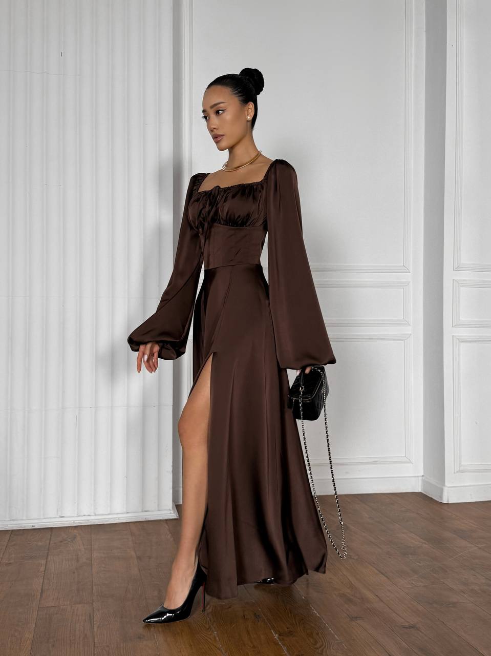 Woman in a brown dress standing against a white wall
