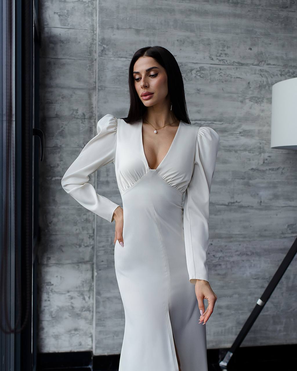 Woman wearing a white dress with long sleeves against a gray wall.