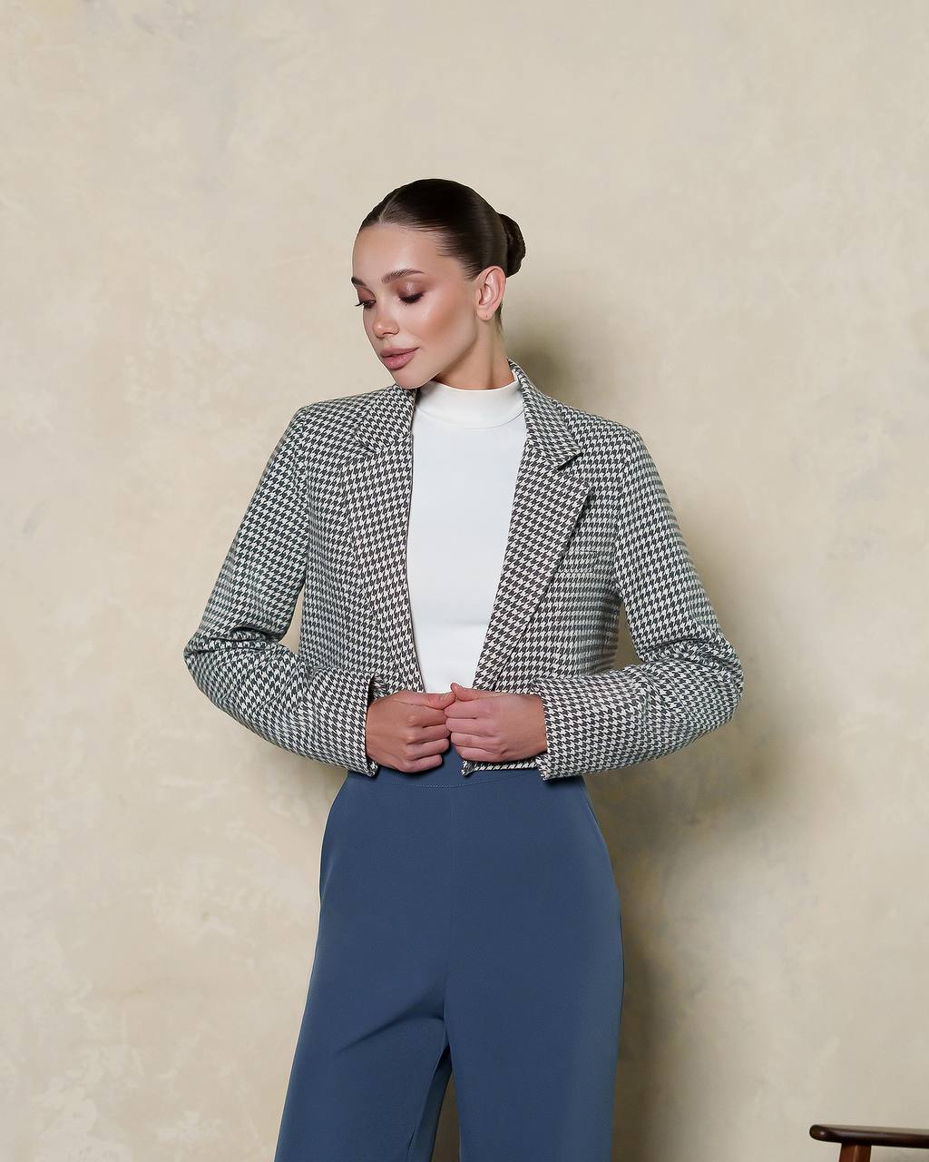 Woman wearing a checkered blazer and blue pants against a beige background