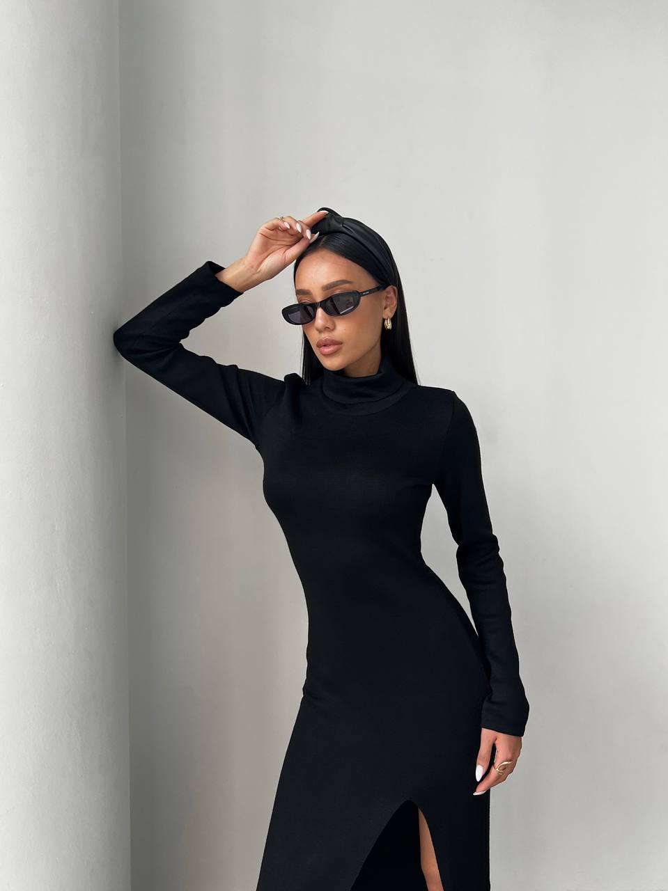 Woman wearing a black long-sleeve dress and sunglasses against a gray background