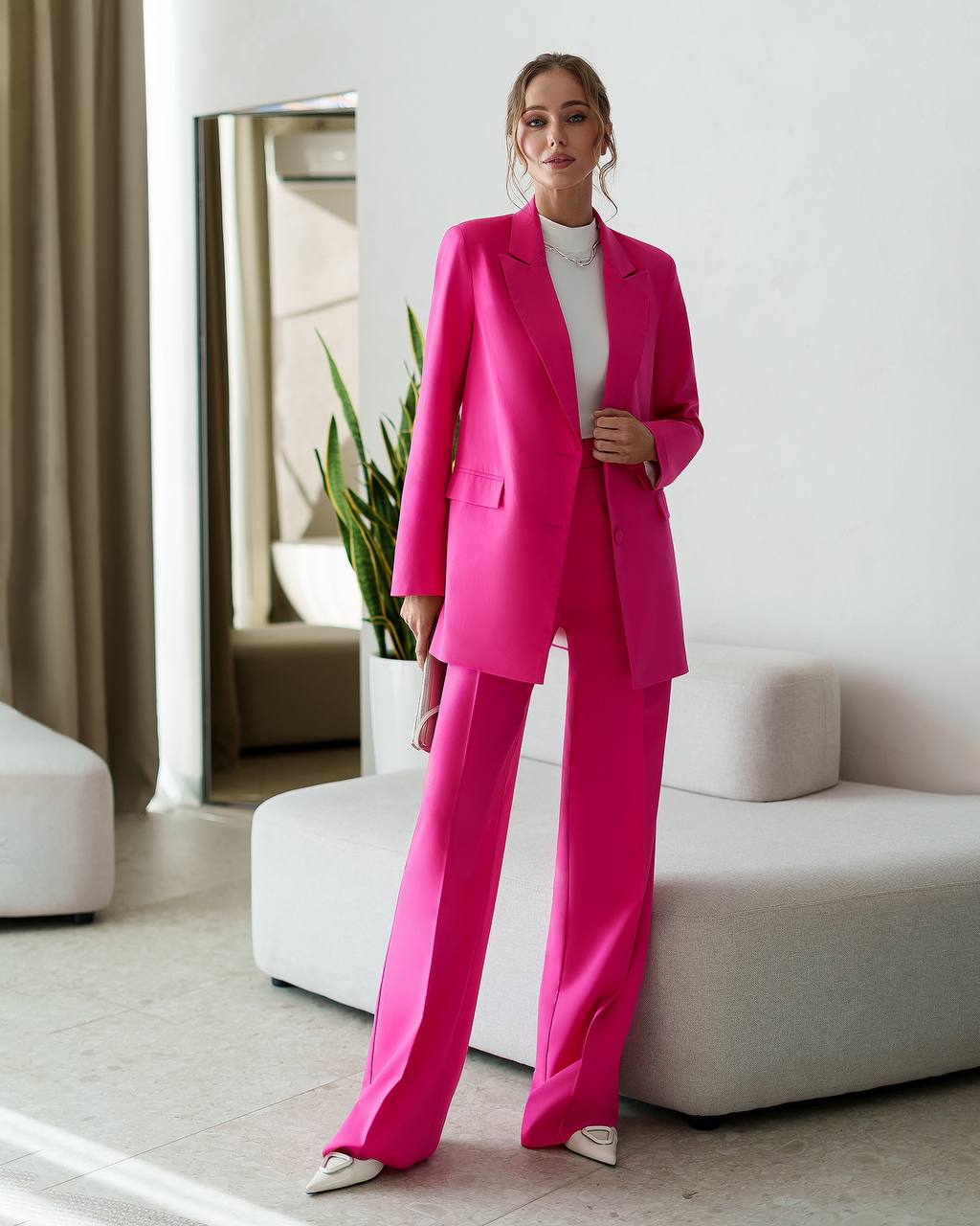 Woman in a bright pink suit standing in a modern living room.