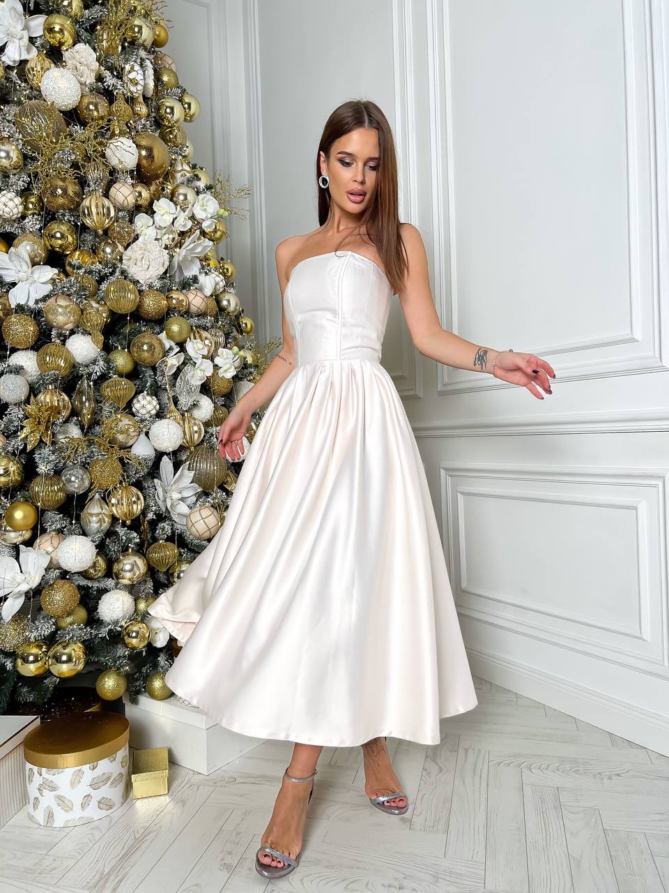 Woman in a white strapless dress standing in front of a decorated Christmas tree.