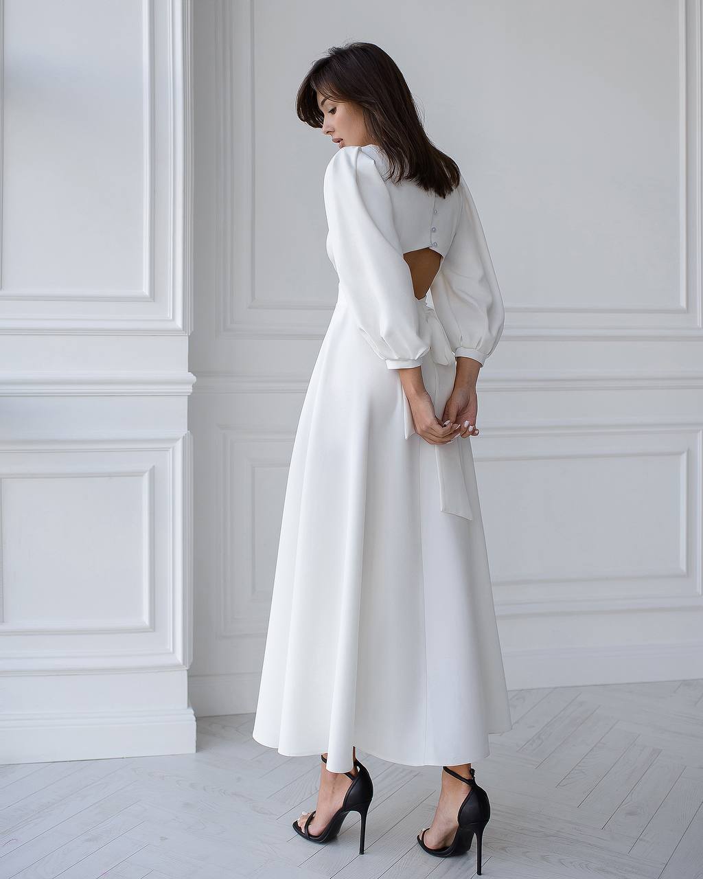 Woman wearing a white dress with cut-out back in a minimalistic room.