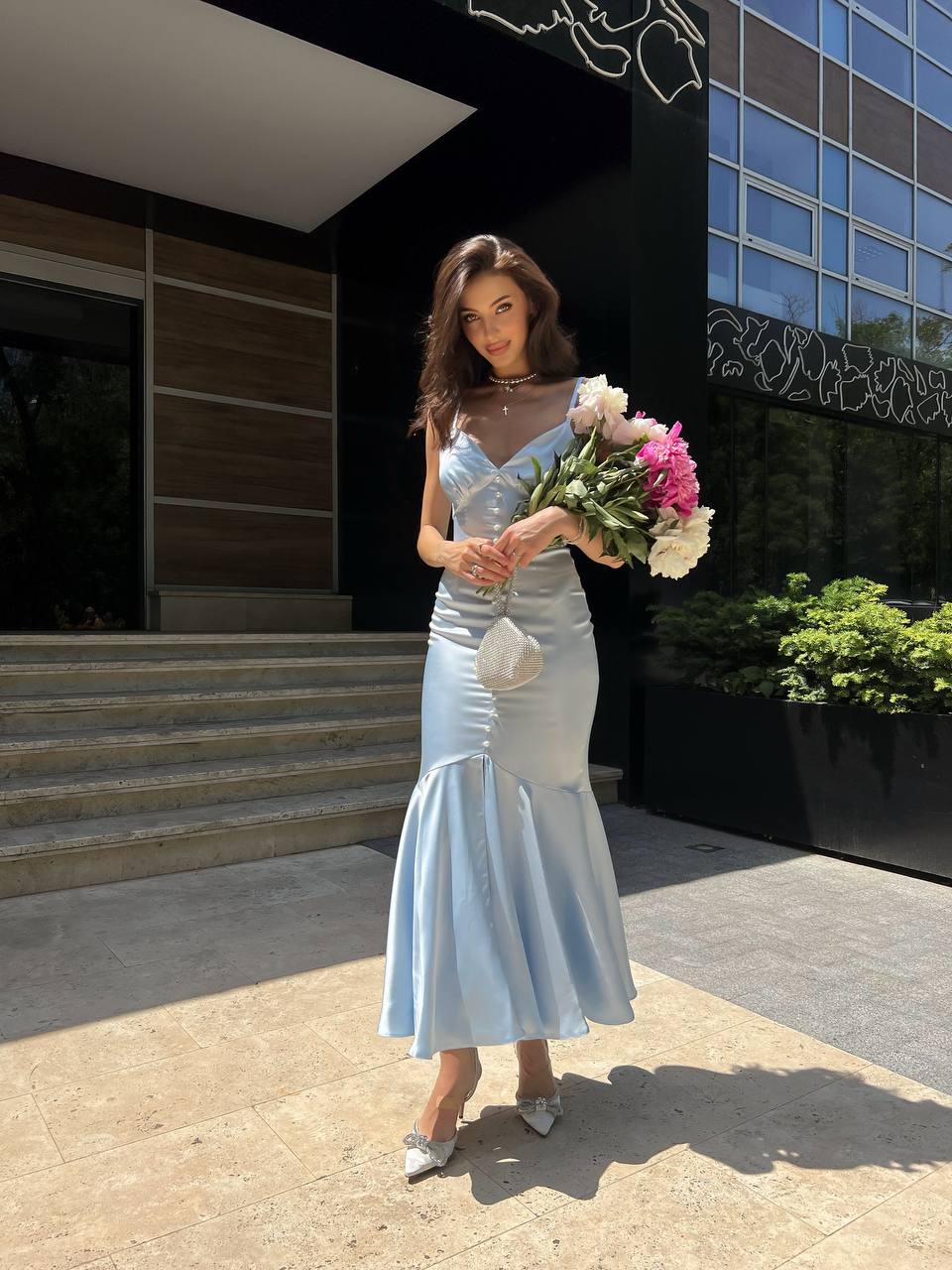 Woman in a light blue dress holding flowers outside a building