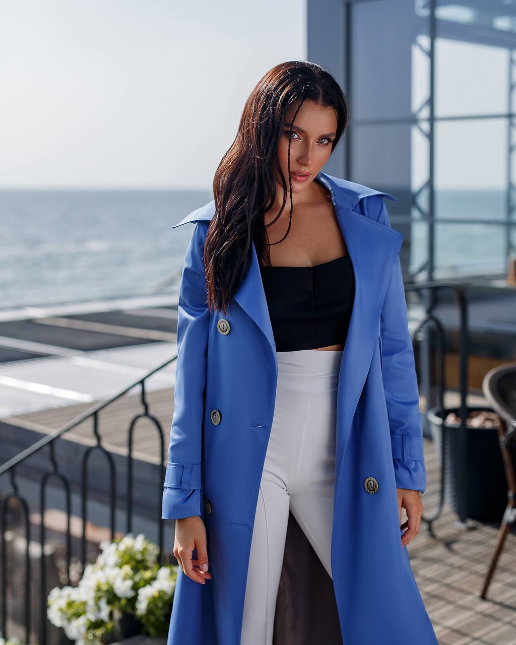 Woman wearing a blue coat standing by a waterfront with ocean view