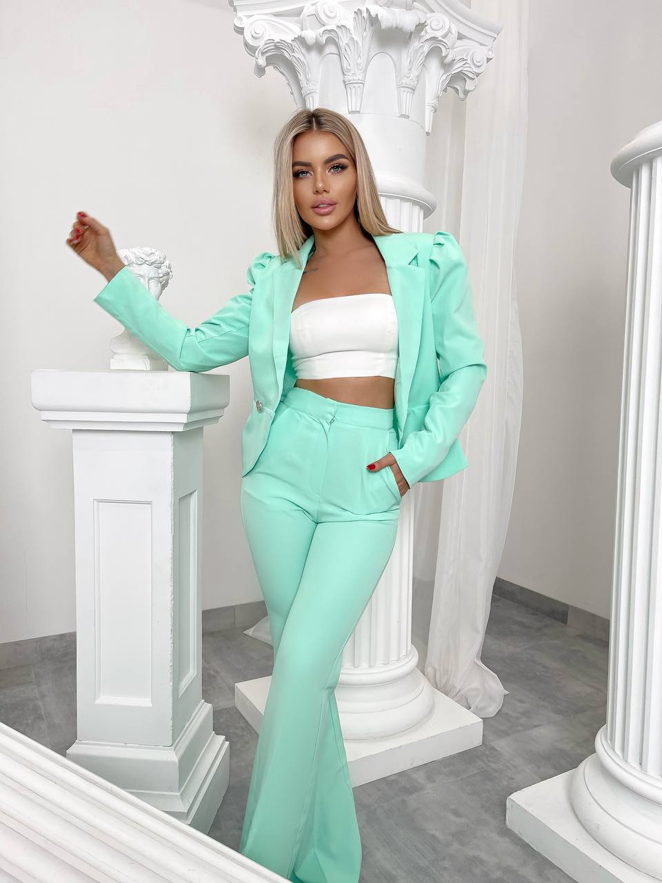 Woman in a mint green outfit standing in an elegant interior setting with white columns.