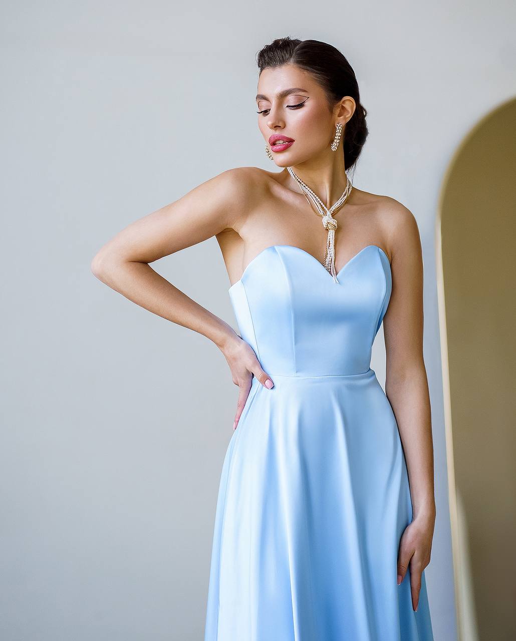 Woman wearing a light blue strapless dress against a plain background