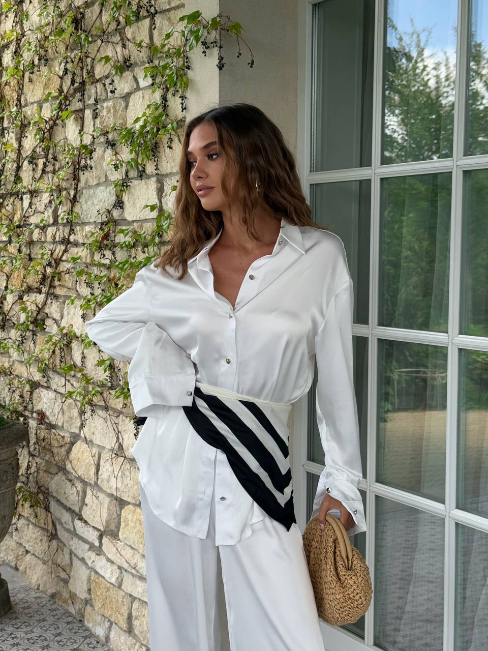 Woman in a white shirt and black and white striped pants standing against a stone wall.