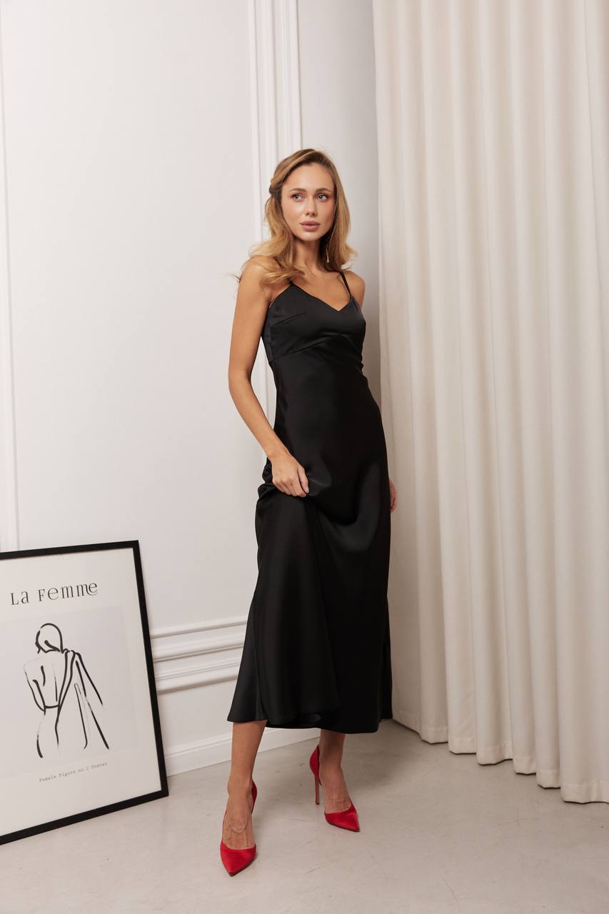 Woman in a black dress with red shoes standing in a room with white walls and curtains.