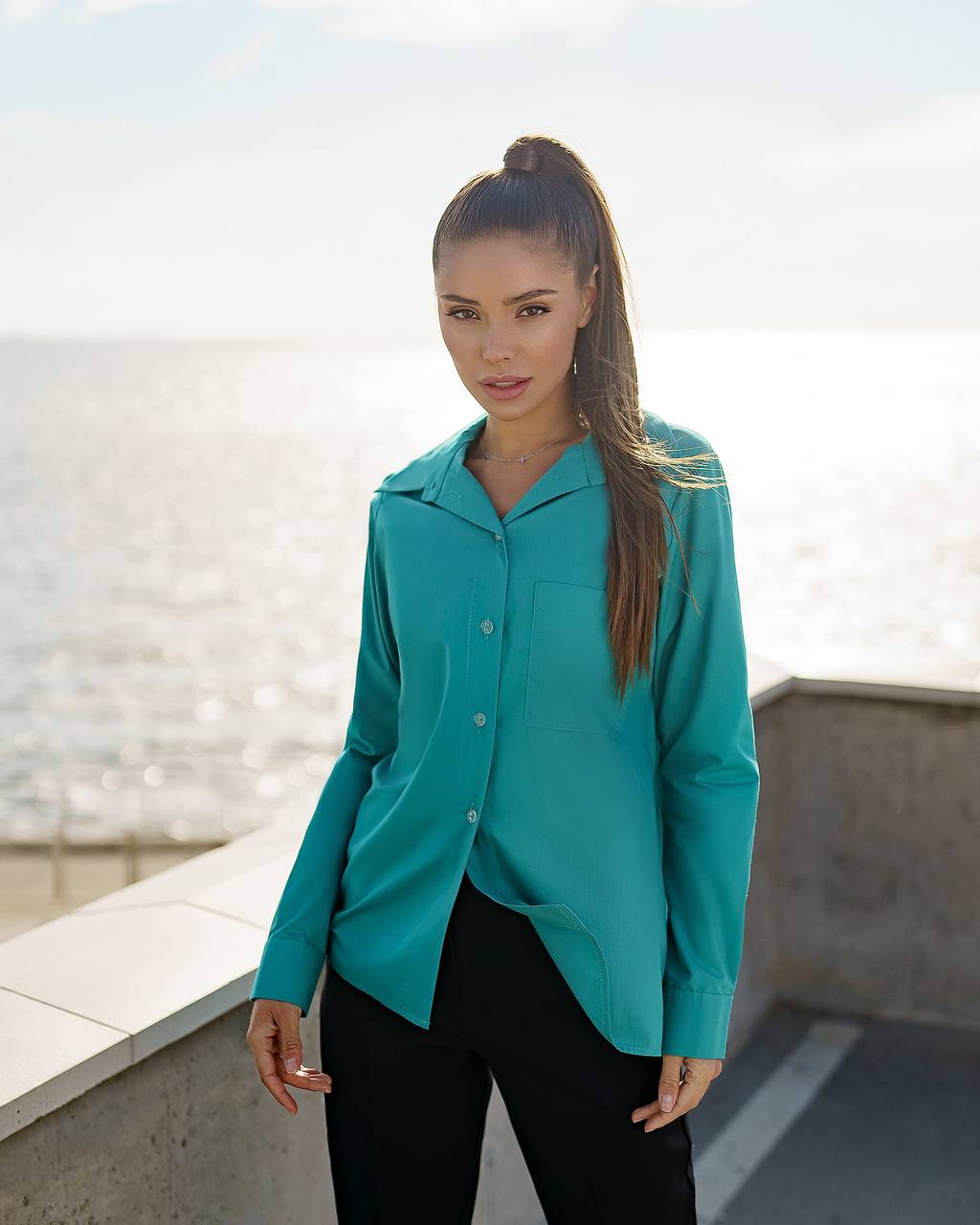 Woman wearing a teal shirt standing on a rooftop with a cityscape background