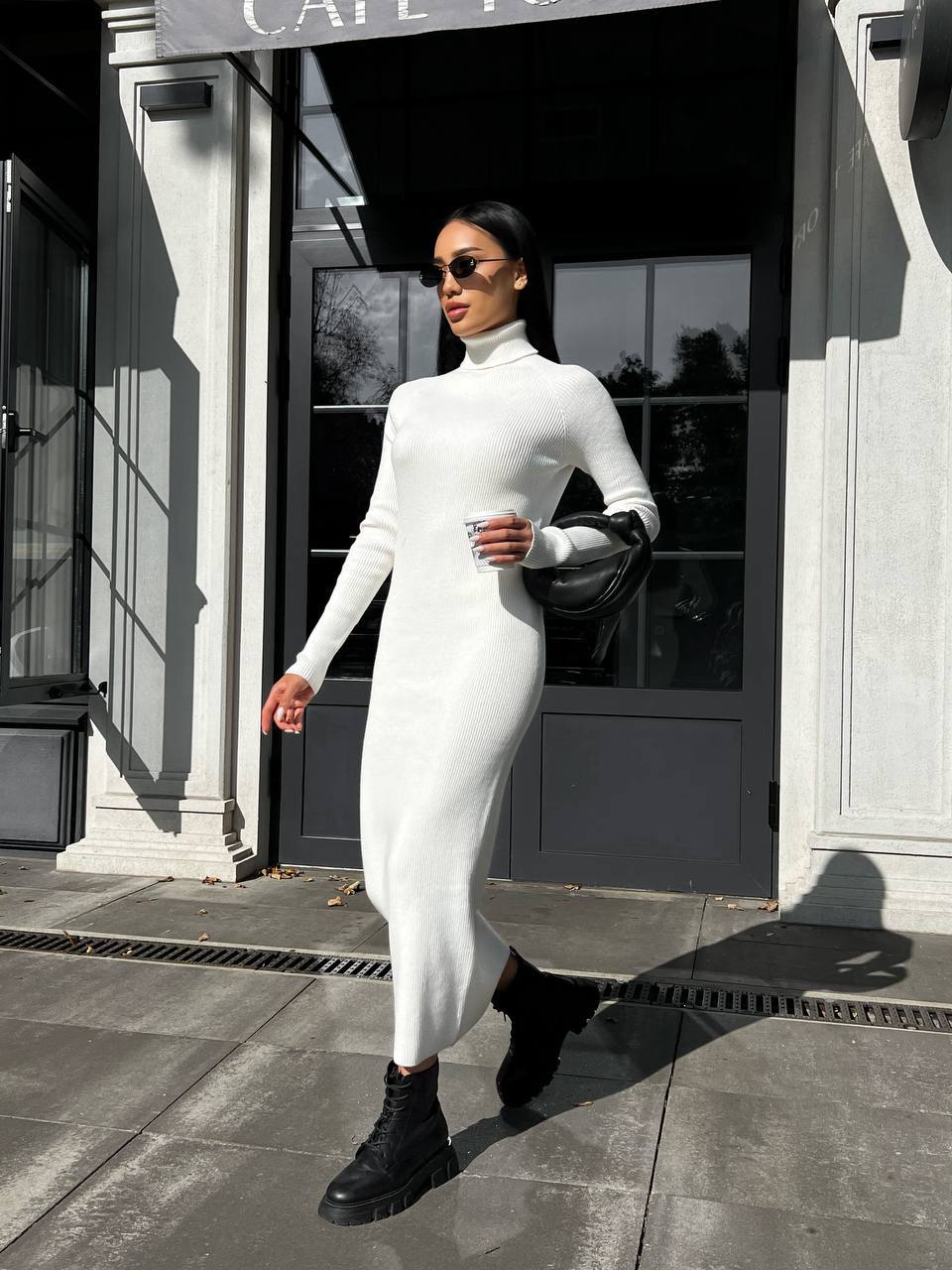 Woman in a white dress and black boots walking outside a building.