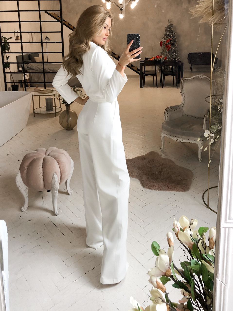 Woman in a white outfit taking a mirror selfie in a stylish room with decor elements.