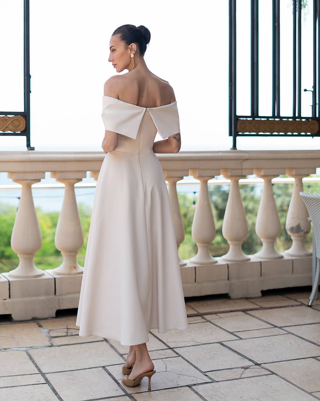Woman in a white off-shoulder dress standing on a balcony with a scenic view.