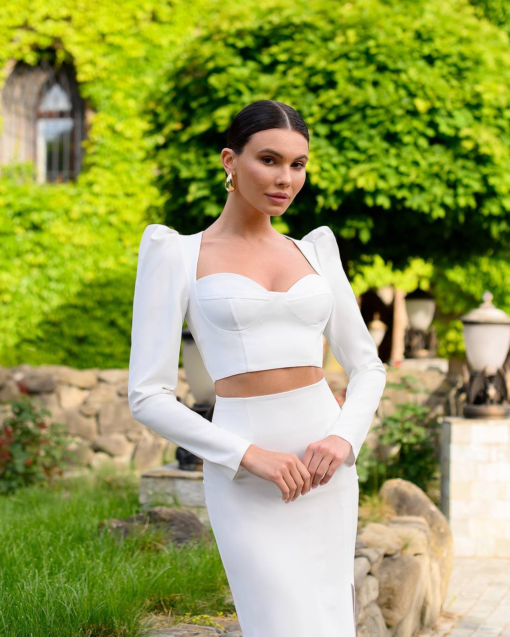 Woman in a white dress standing outdoors with greenery in the background