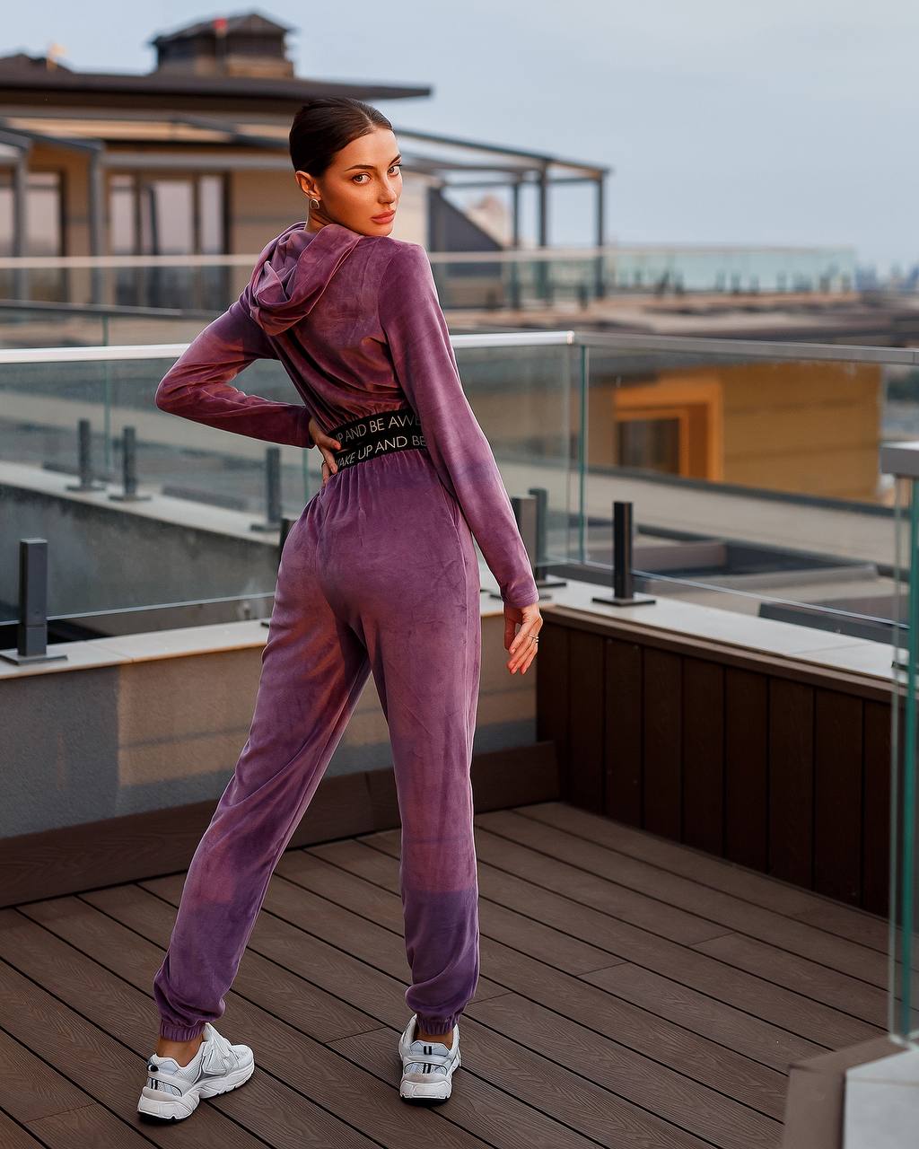 Person wearing a purple tracksuit on a rooftop deck with a cityscape background