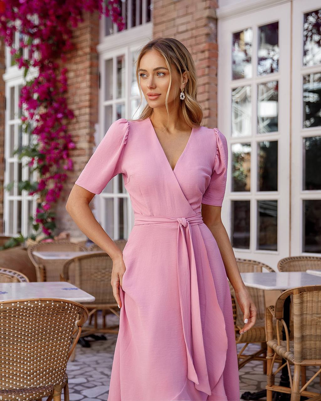 Woman in a pink dress standing outdoors with tables and chairs in the background