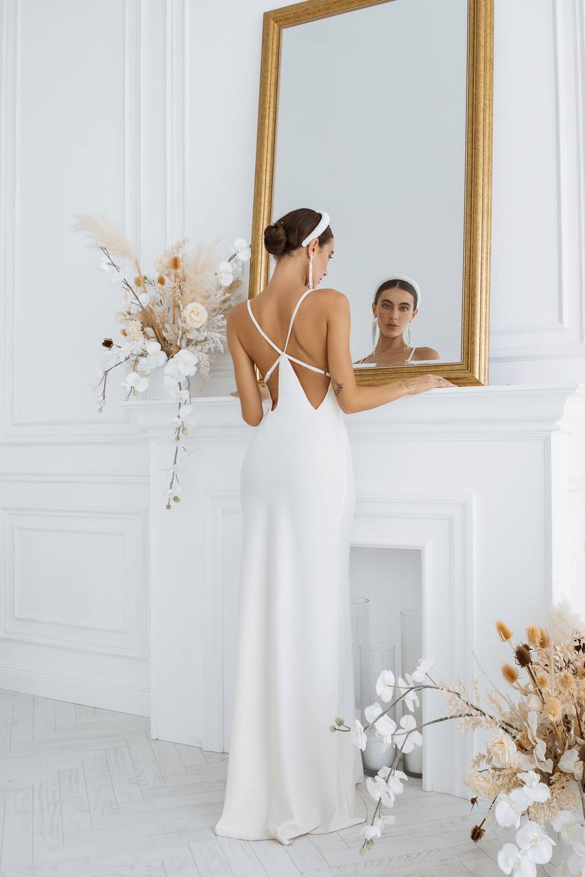 Woman in a white dress standing in front of a mirror in a room with decorative flowers.