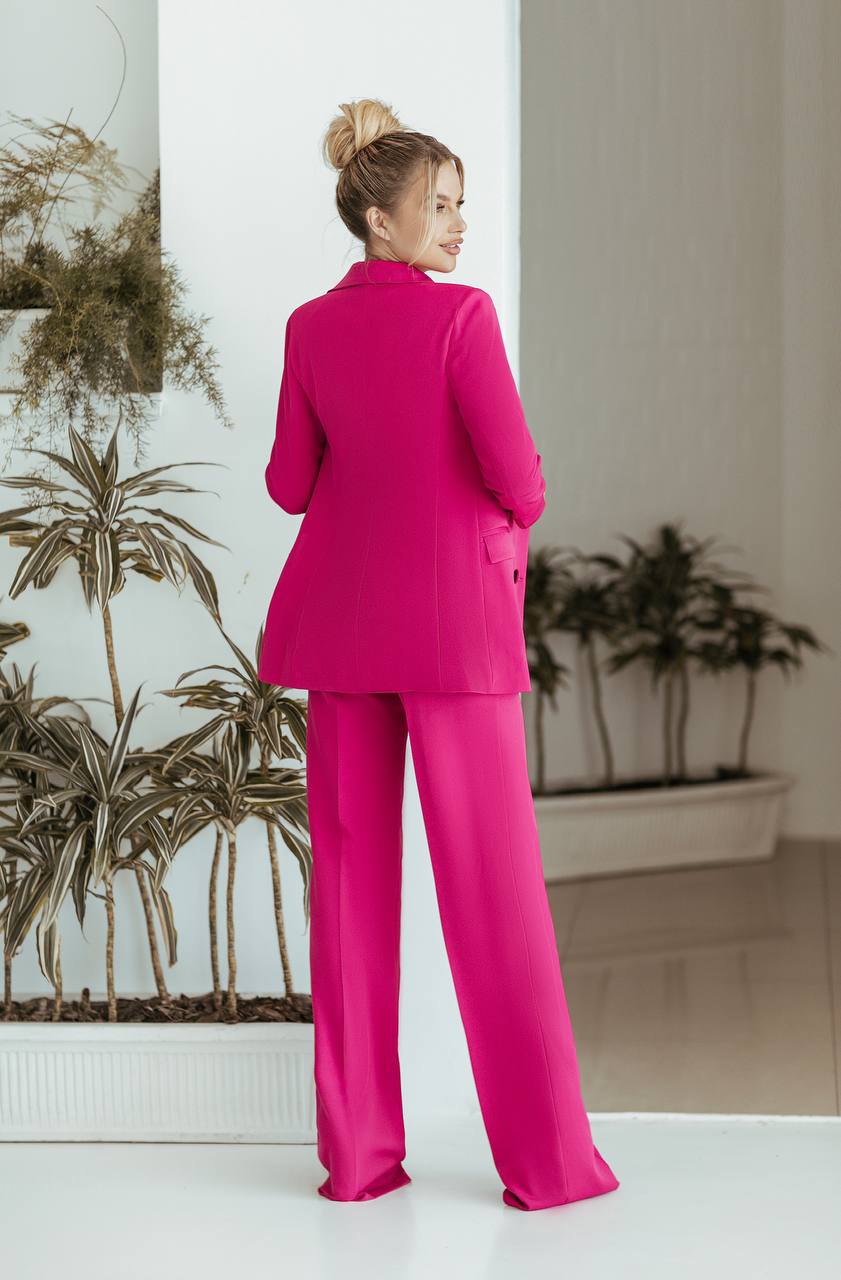 Woman in a bright pink suit standing in a room with plants.