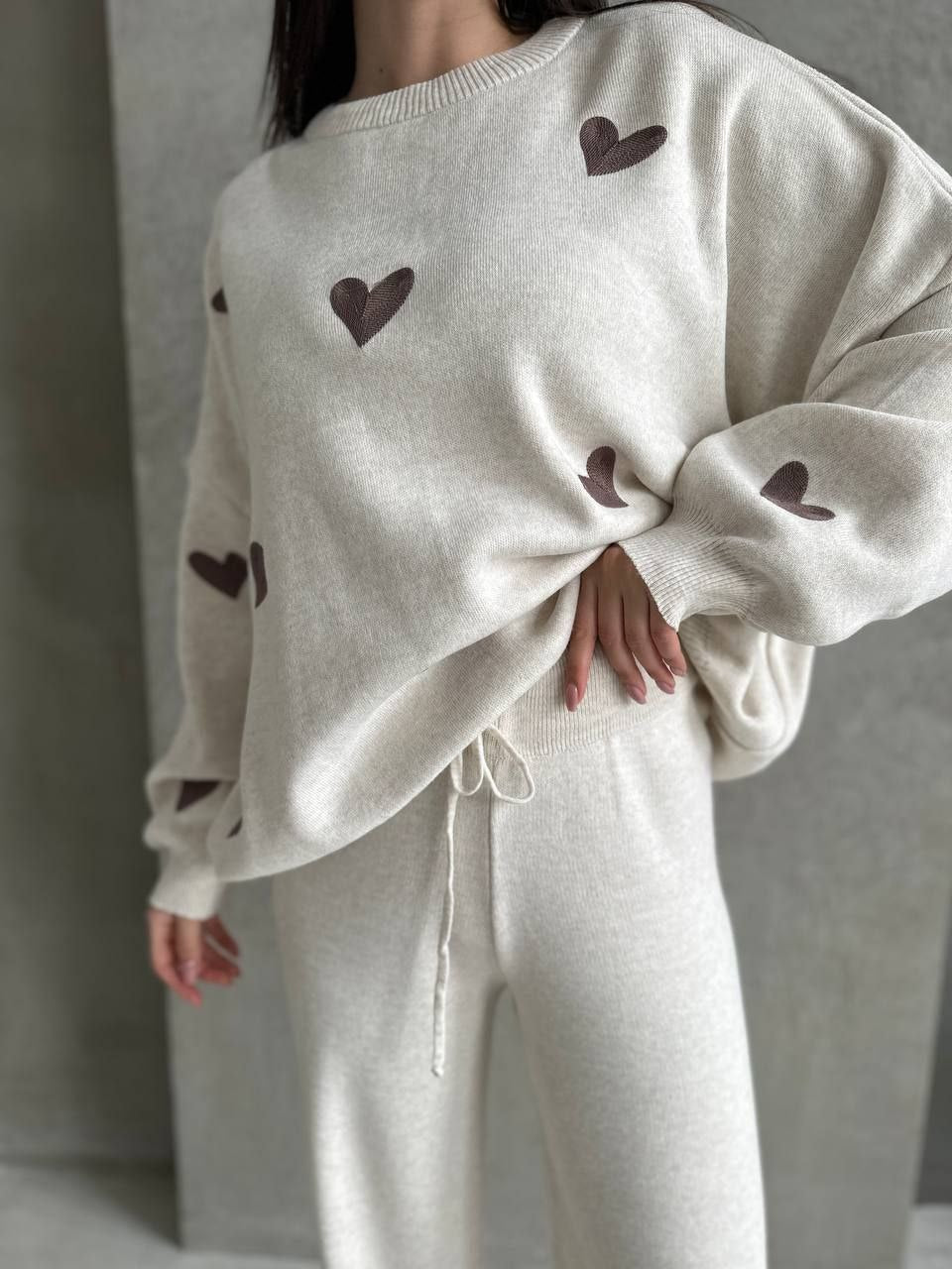 Person wearing a cream-colored sweater with heart patterns and matching pants against a neutral background
