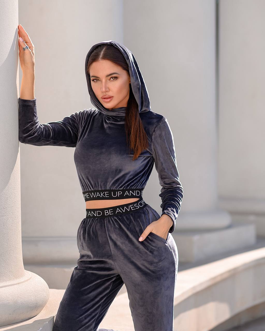 Woman wearing a dark gray tracksuit with a hood, standing against classical architecture.