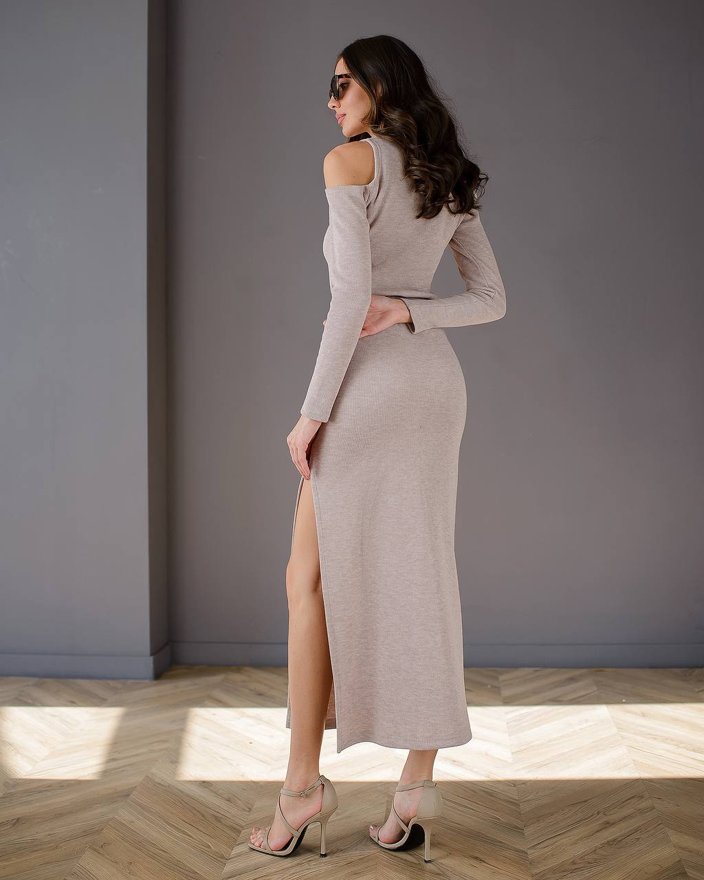 Woman wearing a long, off-shoulder dress with a high slit on a wooden floor.