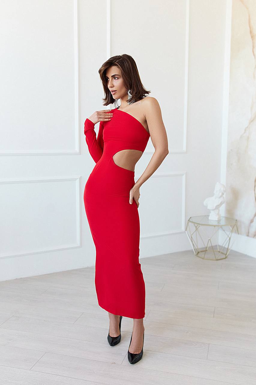 Woman wearing a red one-shoulder dress with cut-out design in a minimalistic room.
