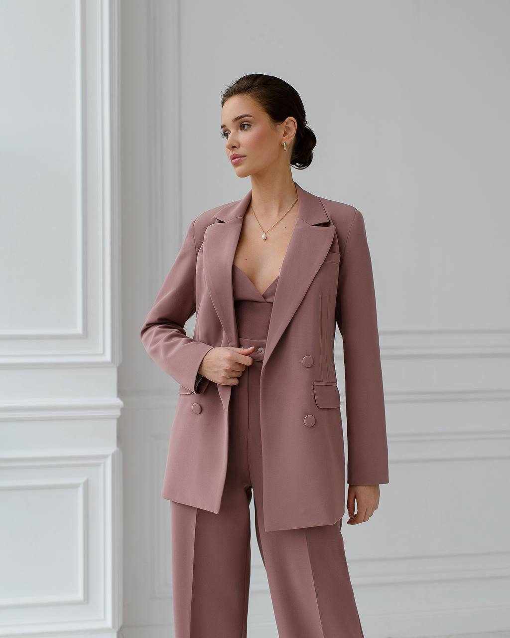Woman wearing a mauve suit standing against a light gray wall.
