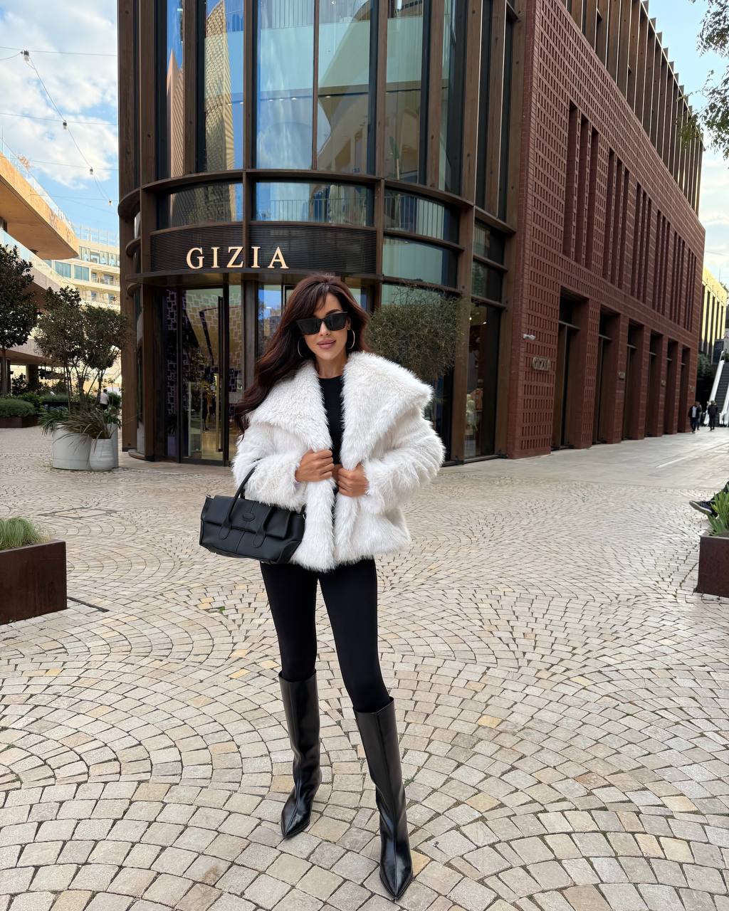 Woman in a white fur coat standing in front of a building with 'Gizia' sign.