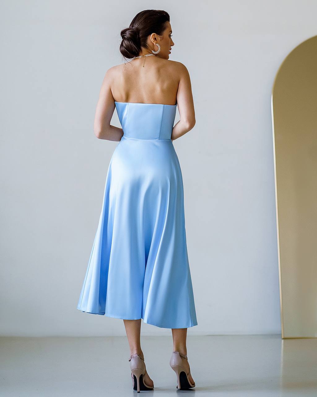 Woman wearing a light blue strapless dress against a white wall.