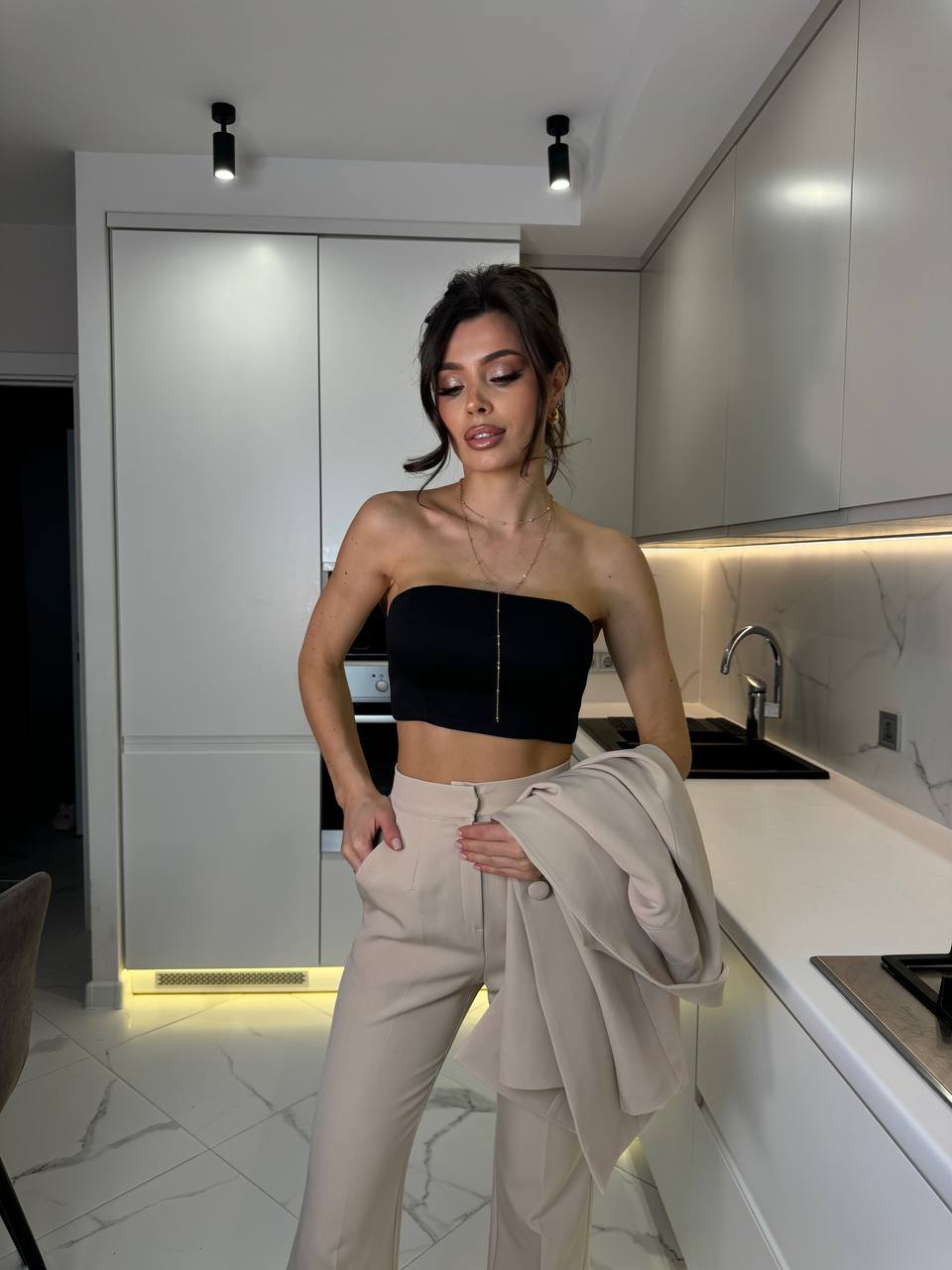 Woman in a black top and beige pants standing in a modern kitchen.