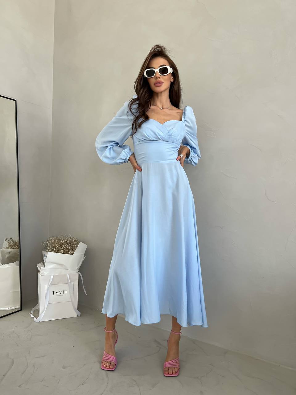 Woman wearing a light blue dress with long sleeves in a minimal indoor setting.