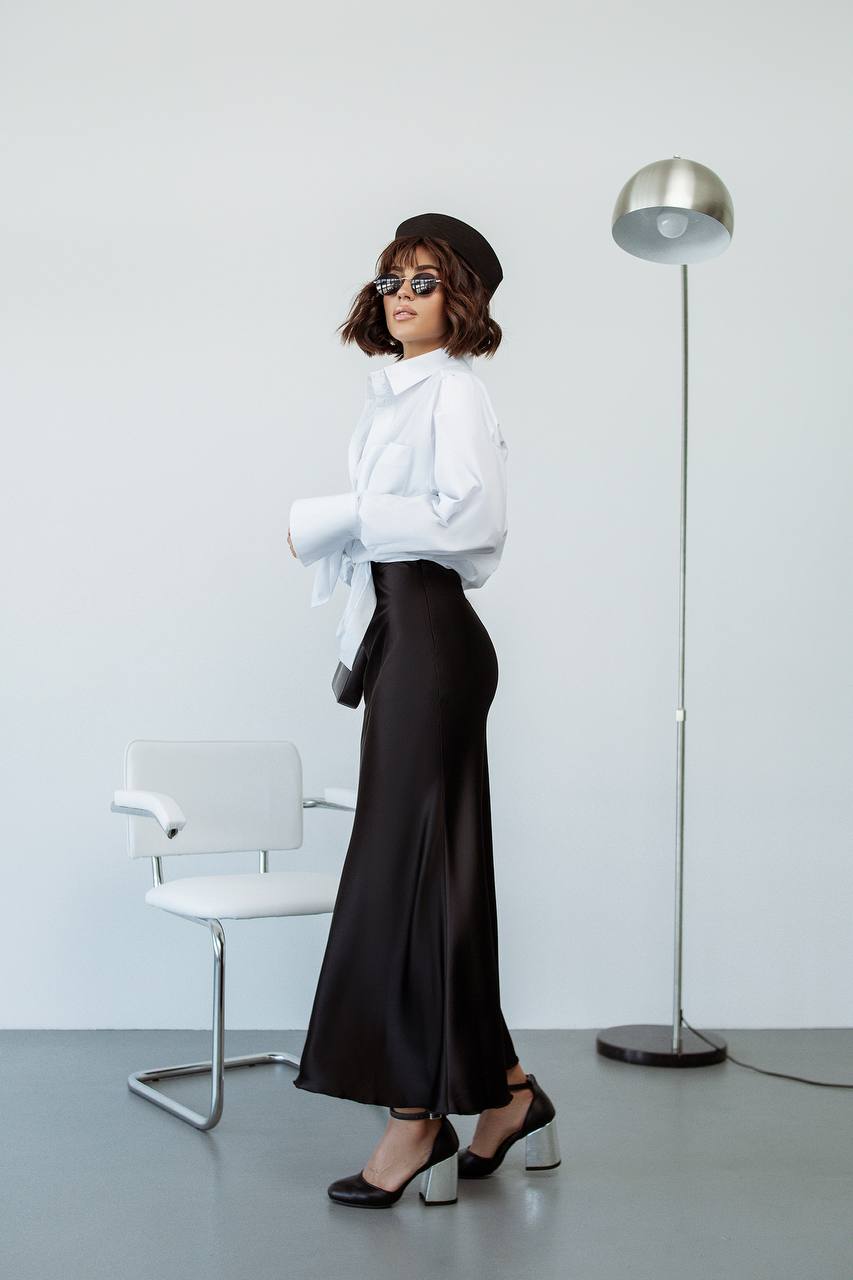 Woman in a white outfit with black skirt standing in a minimalistic room.