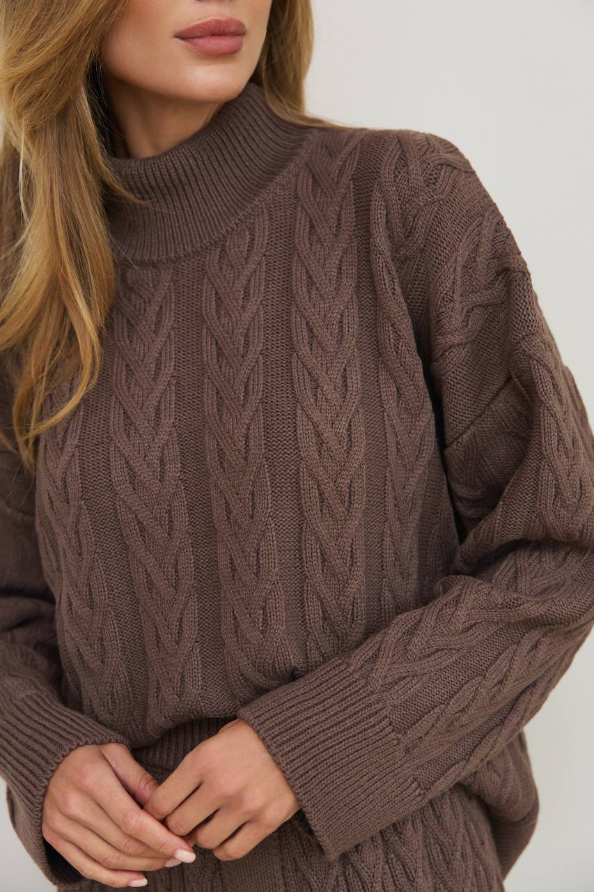 Brown cable knit sweater worn by a person on a light gray background
