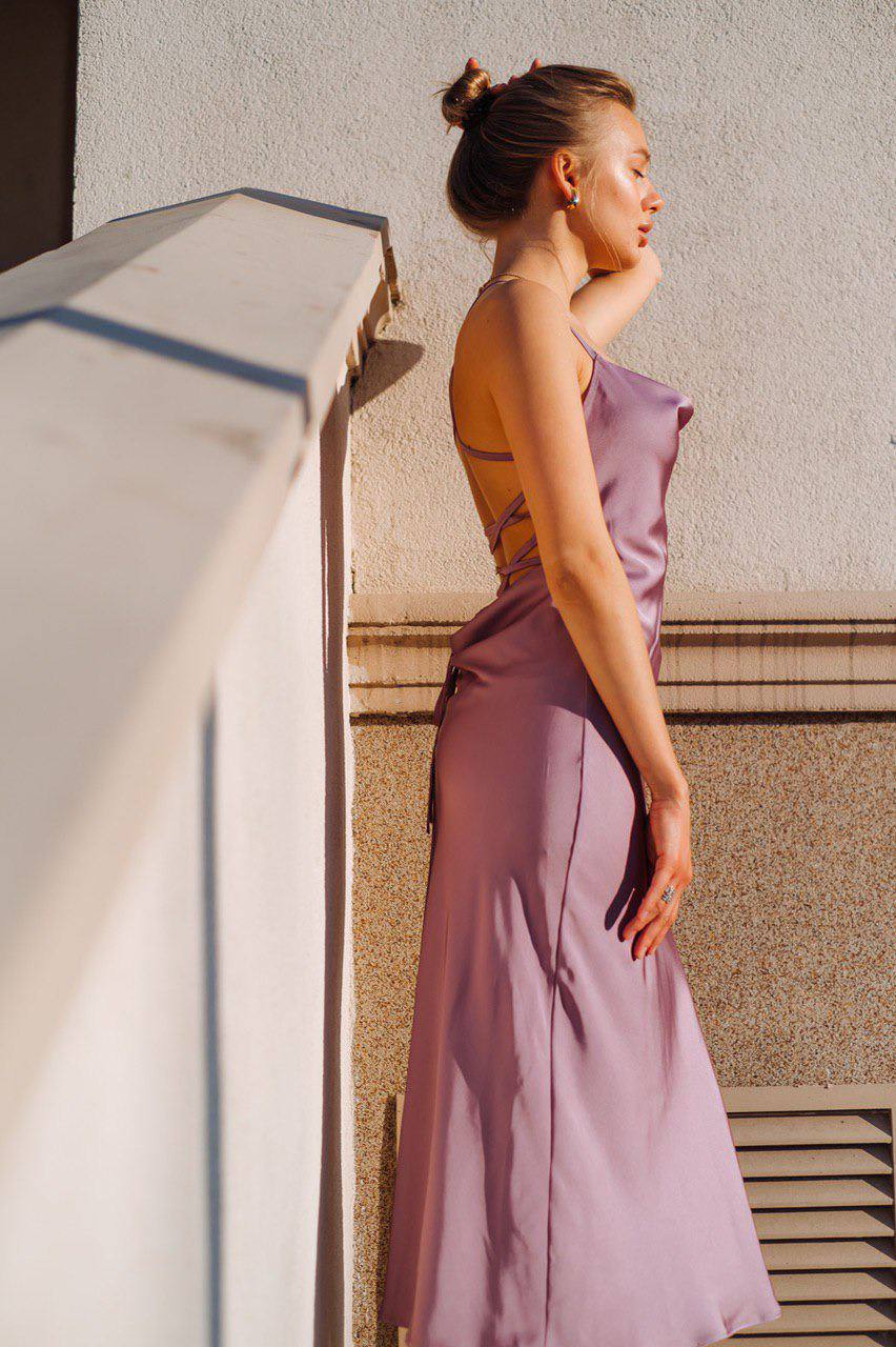 Woman in a purple dress standing against a textured wall.