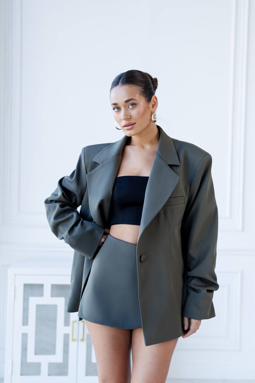 Woman wearing a dark green blazer over a black top and gray shorts against a white background