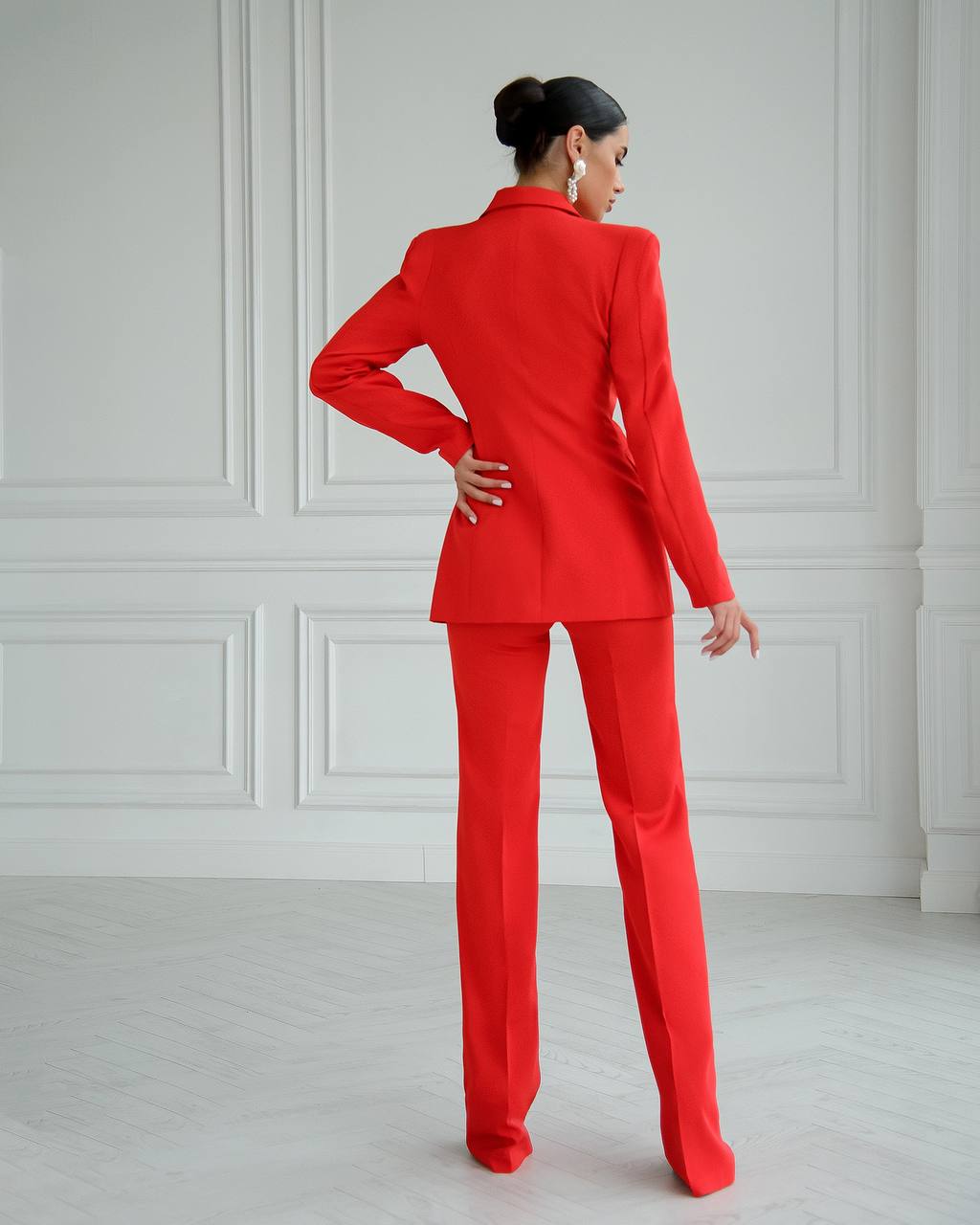 Person wearing a red suit standing against a white paneled wall.