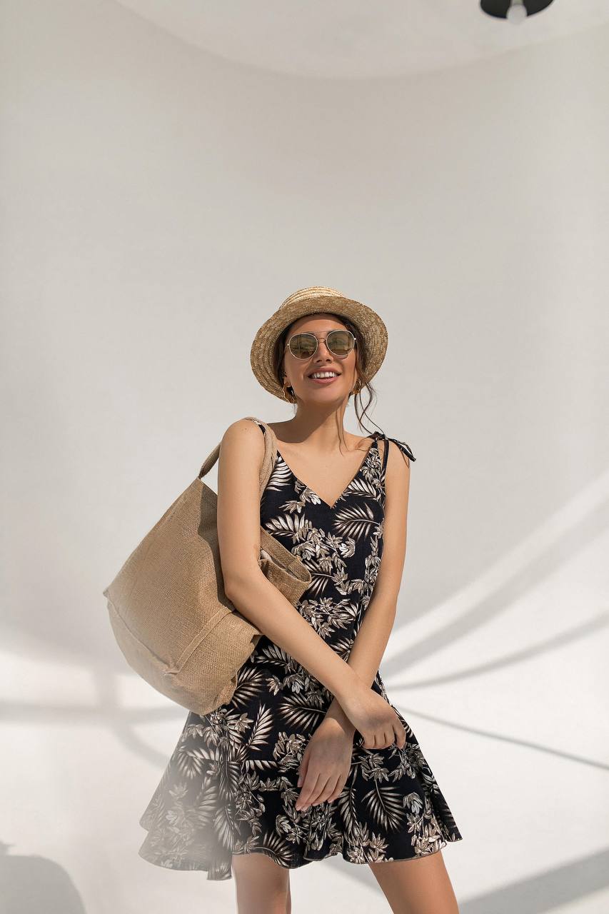 Woman wearing a floral dress and straw hat, holding a beige tote bag against a white background