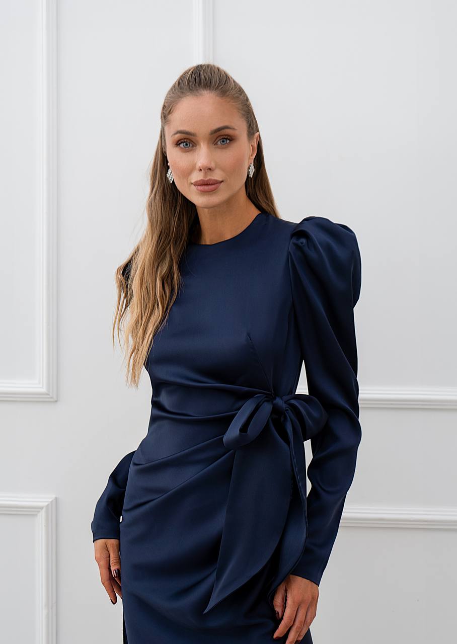 Woman wearing a navy blue dress with puffed sleeves against a white wall