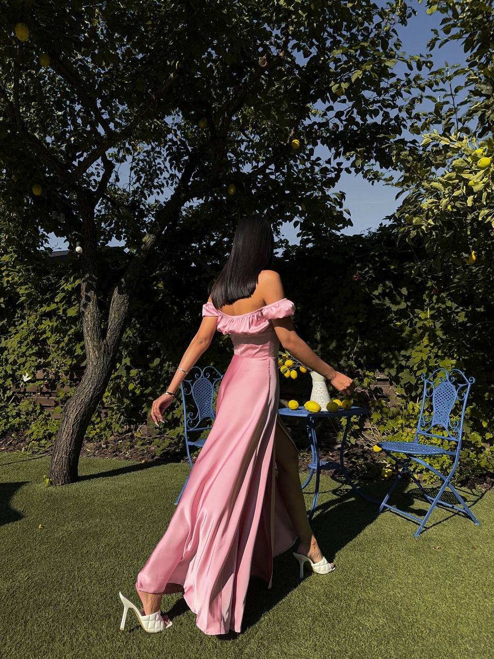 Woman in a pink dress walking in a garden with blue chairs and a table.