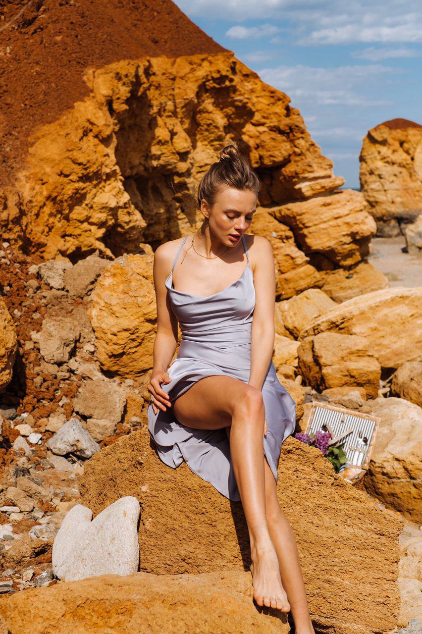 Woman in a light dress sitting on a rocky landscape with red and orange cliffs.
