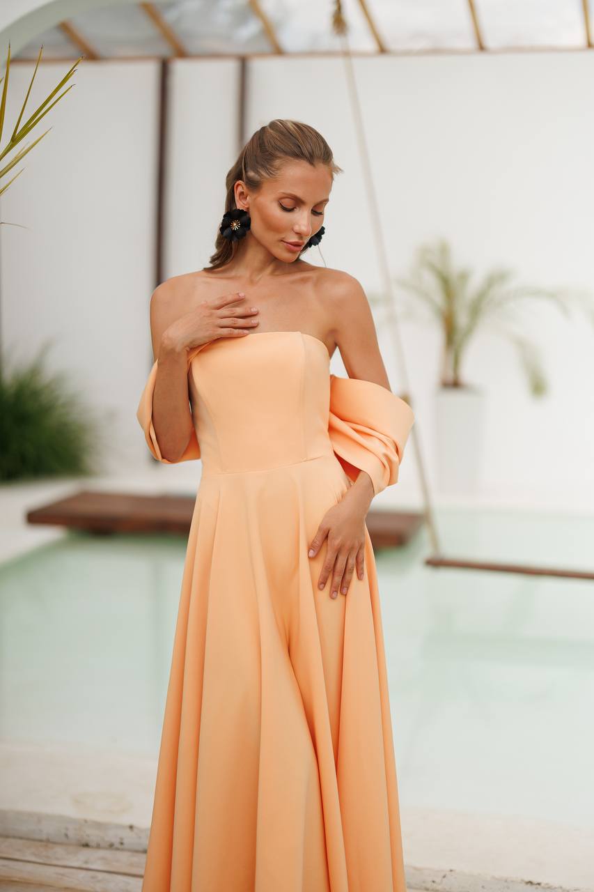 Woman in a peach dress standing outdoors with plants in the background