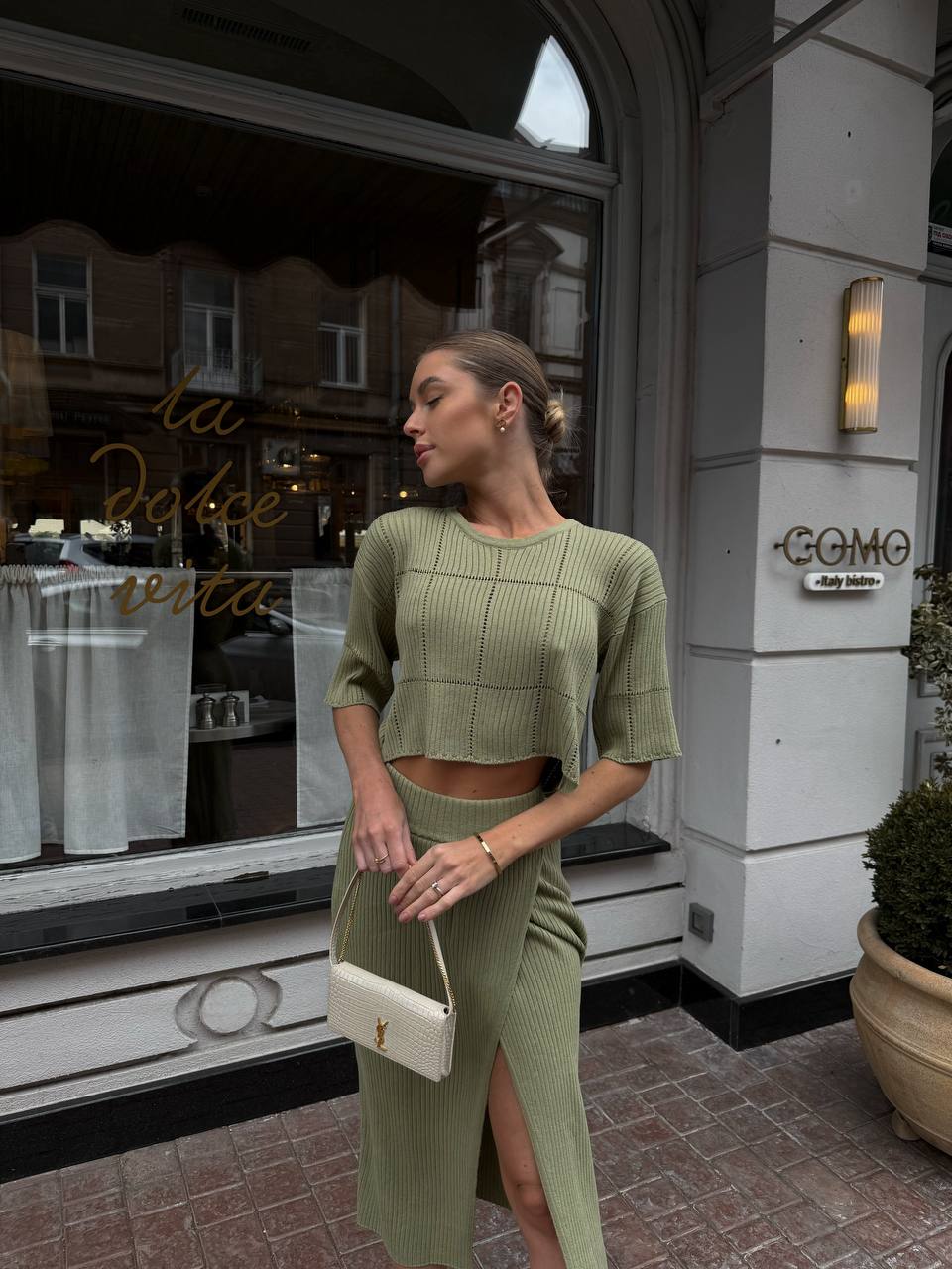 Woman in a green outfit standing in front of a building entrance.