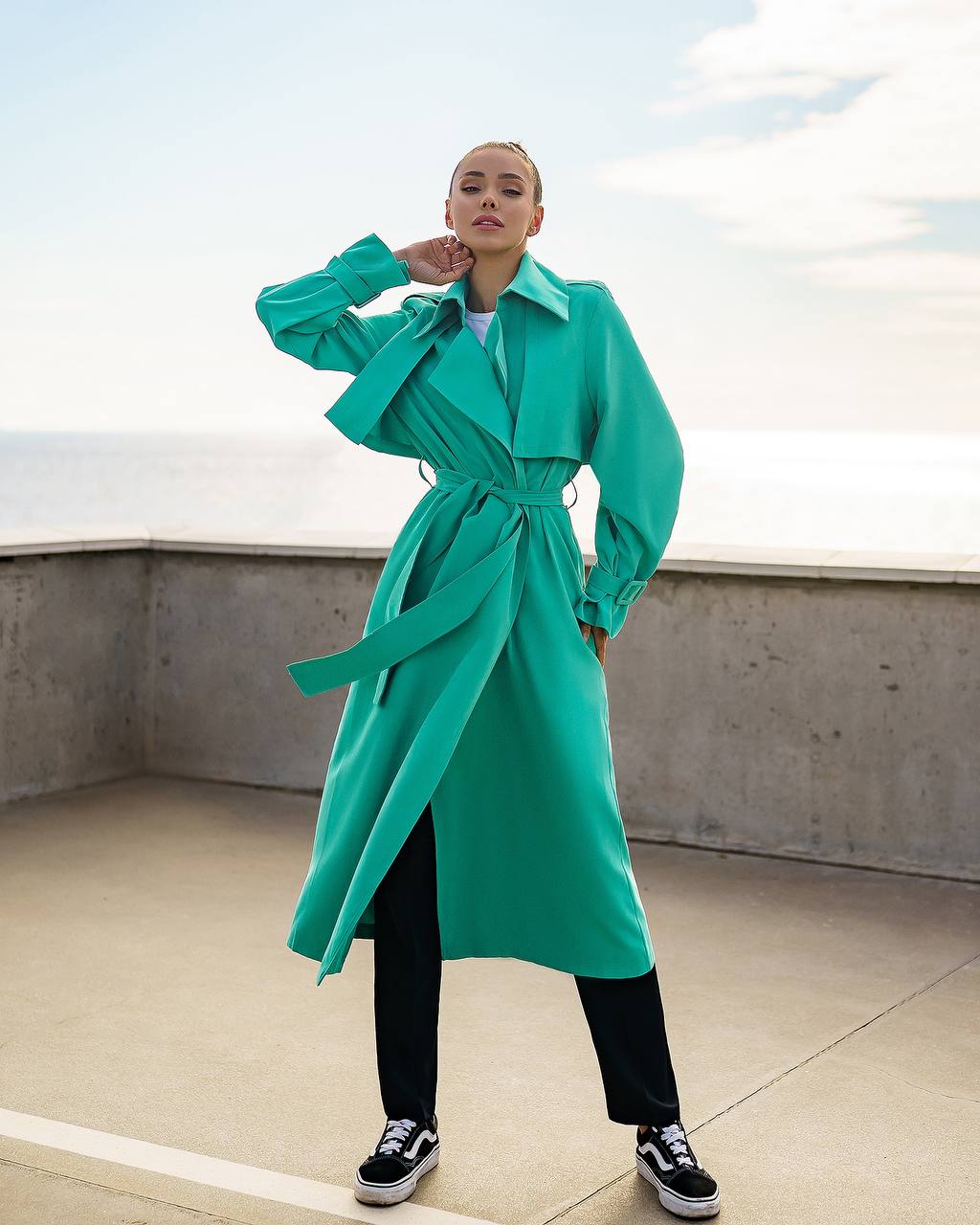 Person wearing a teal trench coat on a rooftop with a clear sky.
