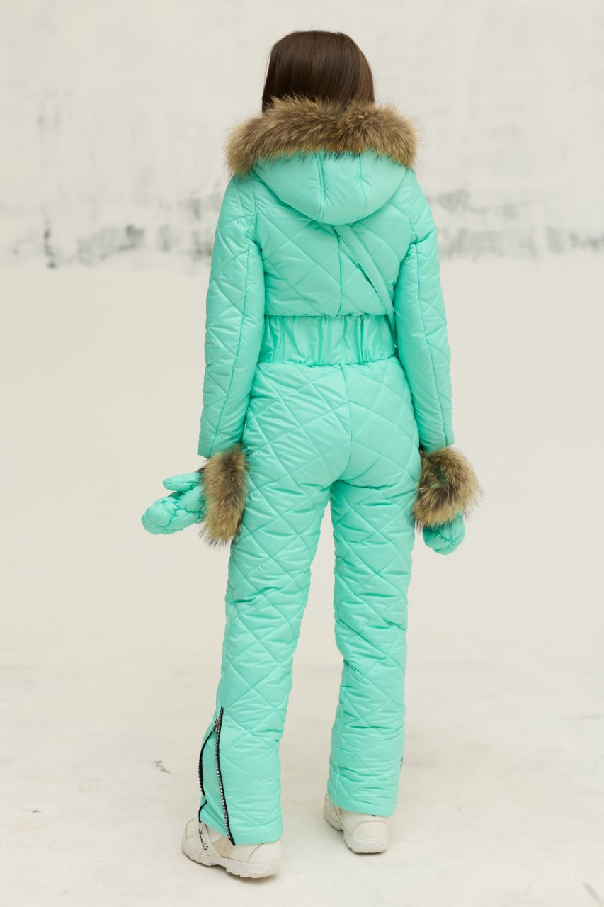 Person wearing a turquoise snowsuit with fur trim on a light background