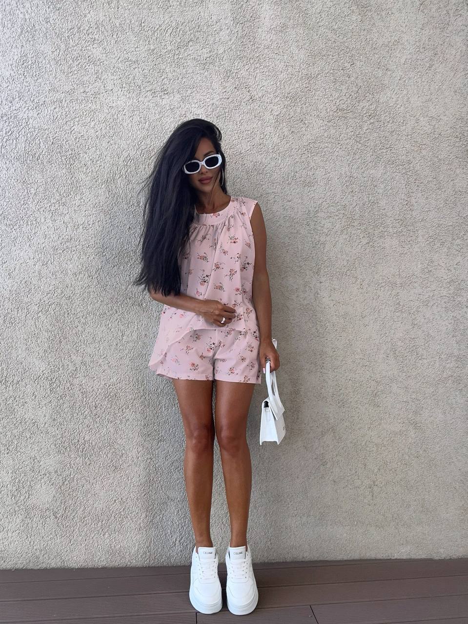 Woman in a pink floral outfit standing against a textured wall.
